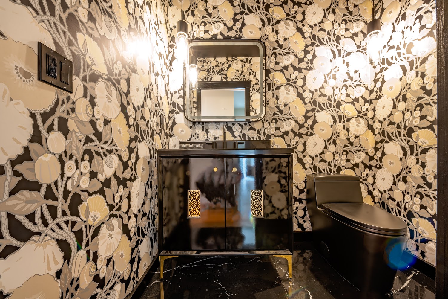 Lillian Powder Room — bold black and cream floral wallpaper, glossy black vanity with gold grille details and black toilet