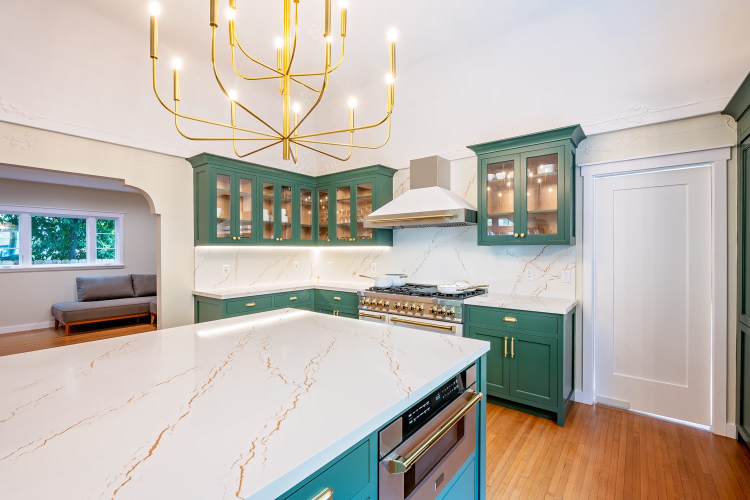 Lillian Kitchen Remodel — angled view across the marble island toward glass-front green cabinets and professional range