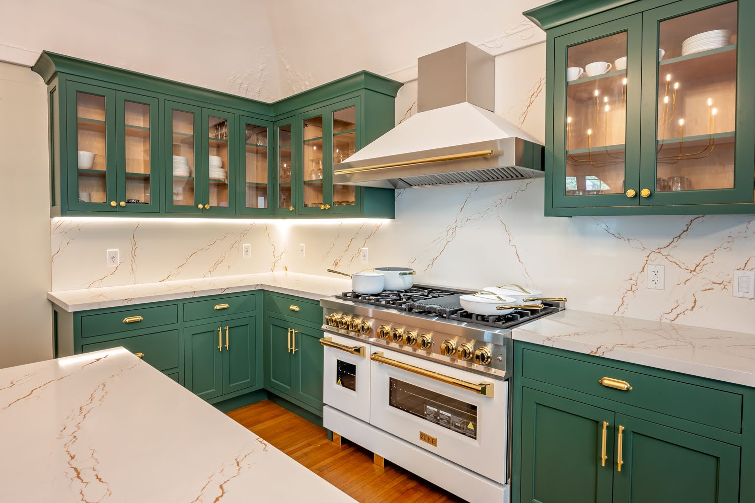 LIS kitchen remodel with deep green cabinetry, gold hardware, marble-look counters and backsplash, and a professional range with white and gold hood